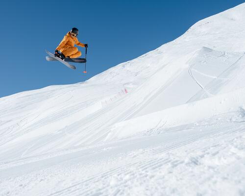 Ein Freeride Skifahrer im orangenen Skianzug springt in die Luft