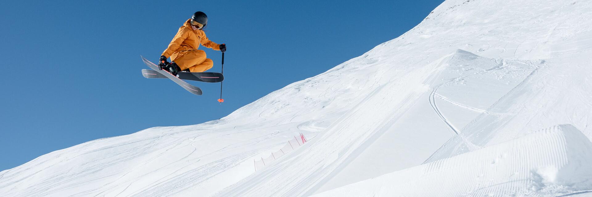 Ein Freeride Skifahrer im orangenen Skianzug springt in die Luft