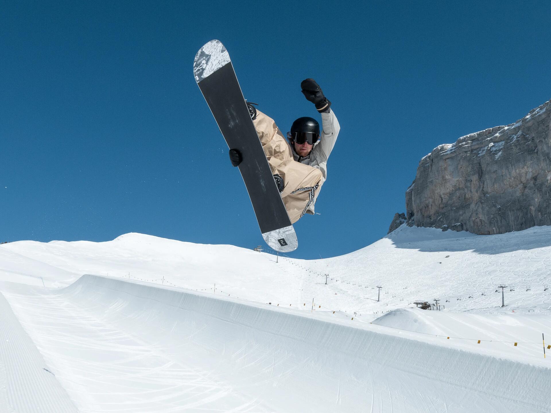 Mężczyzna w kasku i goglach snowboardowych wykonujący trik w snowparku na snowboardzie