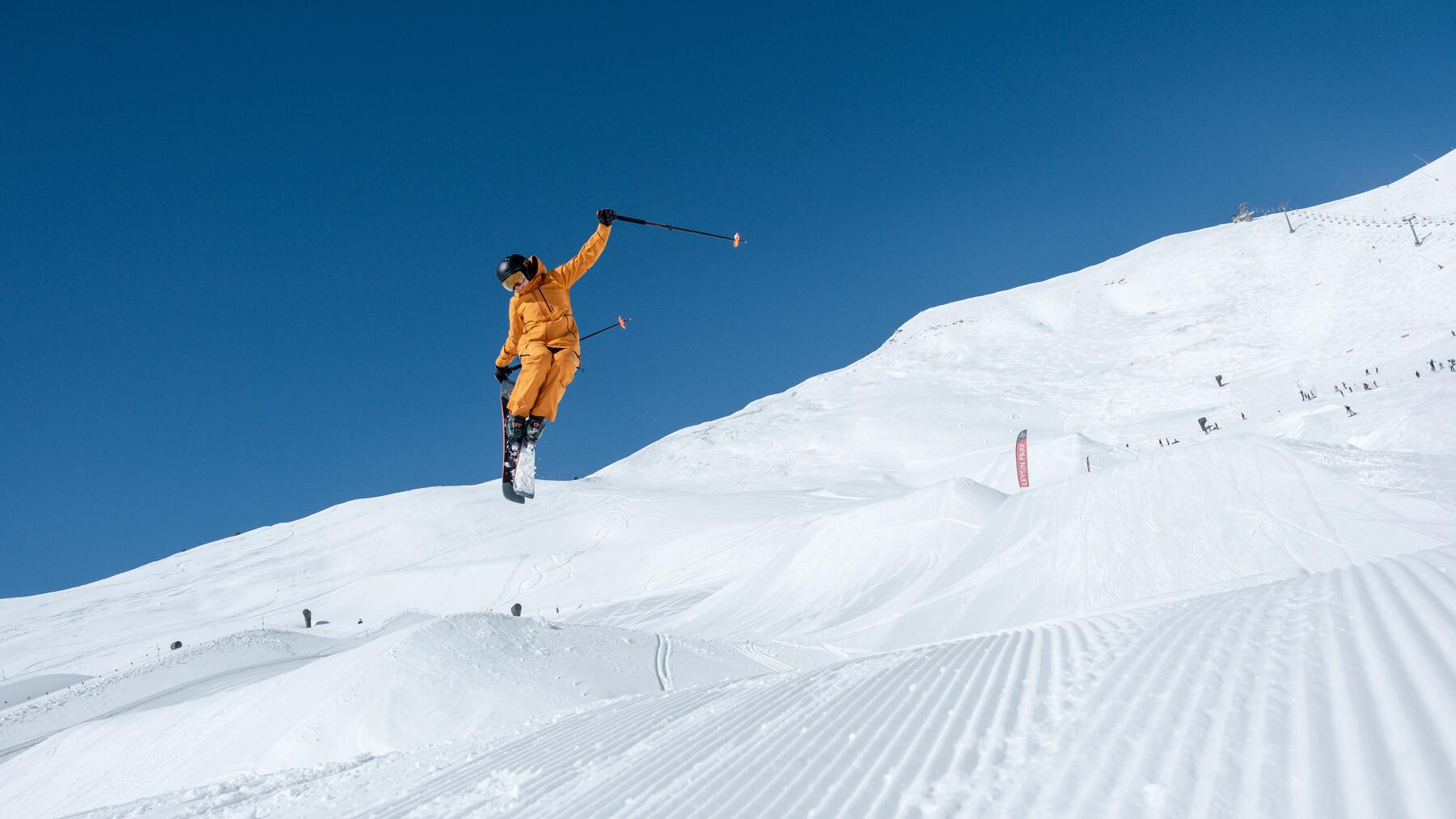 Freeriderin mit orangenem Skianzug springt in die Luft.
