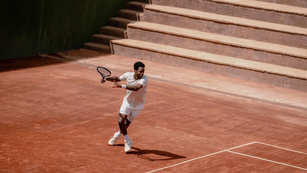 Der Tennisspieler Gaël Monfils in weißer Kleidung holt auf einem Sandplatz zum Vorhand-Schlag aus.