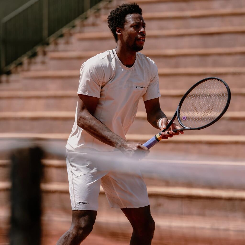 Nahaufnahme eines Tennisspielers in weißer Sportkleidung, der aufmerksam den Schläger mit beiden Händen hält.