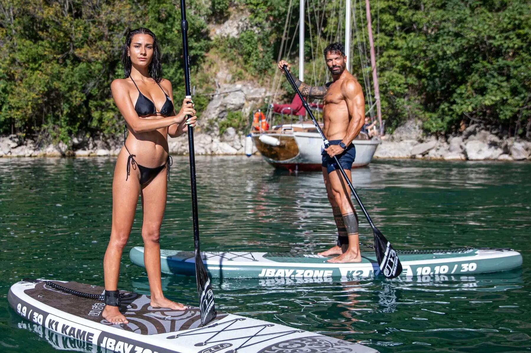 Kobieta i mężczyzna w strojach kąpielowych stojący na deskach stand up paddle trzymając wiosła
