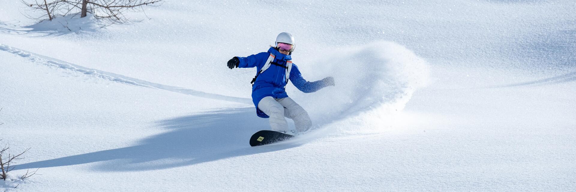 Kobieta w kasku i w goglach jeżdżąca na snowboardzie