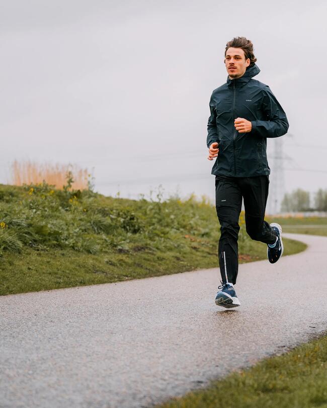 Mann joggt auf gewundenem Weg, grauer Himmel, grüne Wiese, dunkle Sportkleidung, nasse Straße, frische Atmosphäre.