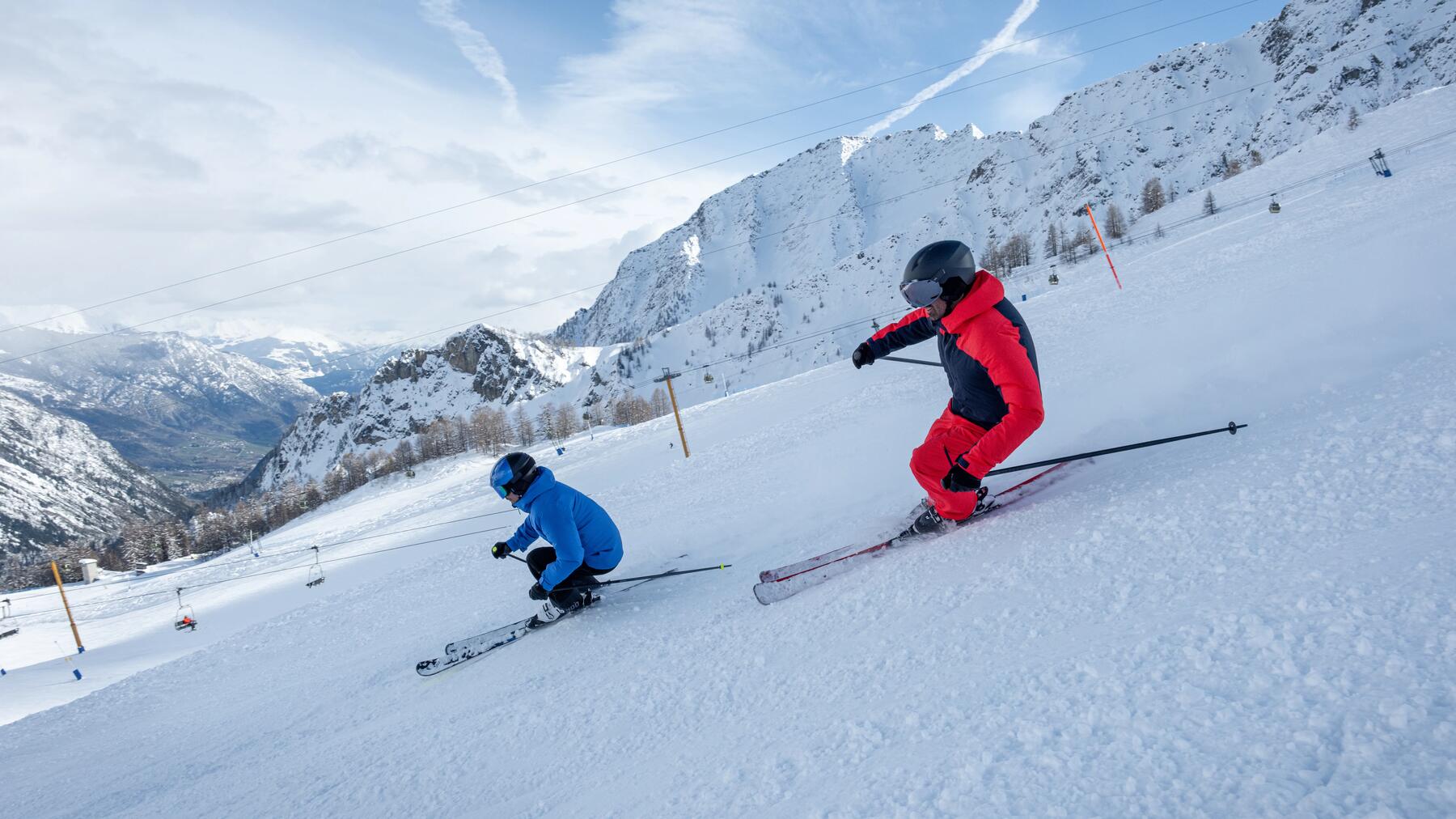 Zwei Skifahrer in roter und blauer Skibekleidung fahren den Berg mit ihren Skiern runter.