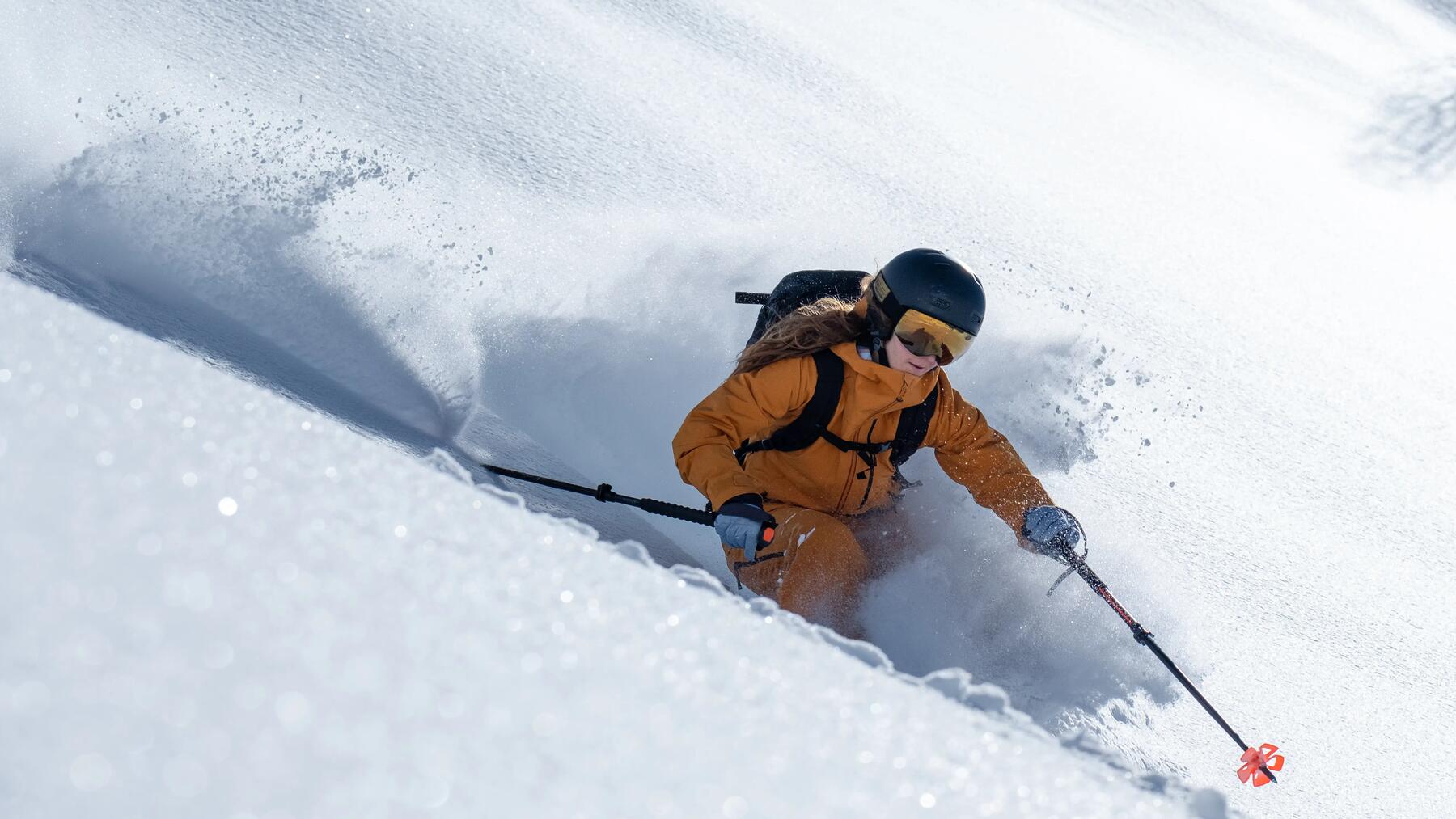 Freeride-Fahrerin im orangenen Skianzug fährt durch tiefen Pulverschnee.