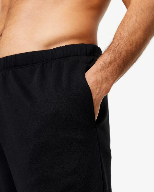 Nahaufnahme: Hand eines oberkörperfreien Mannes in der offenen Seitentasche einer schwarzen Sporthose.