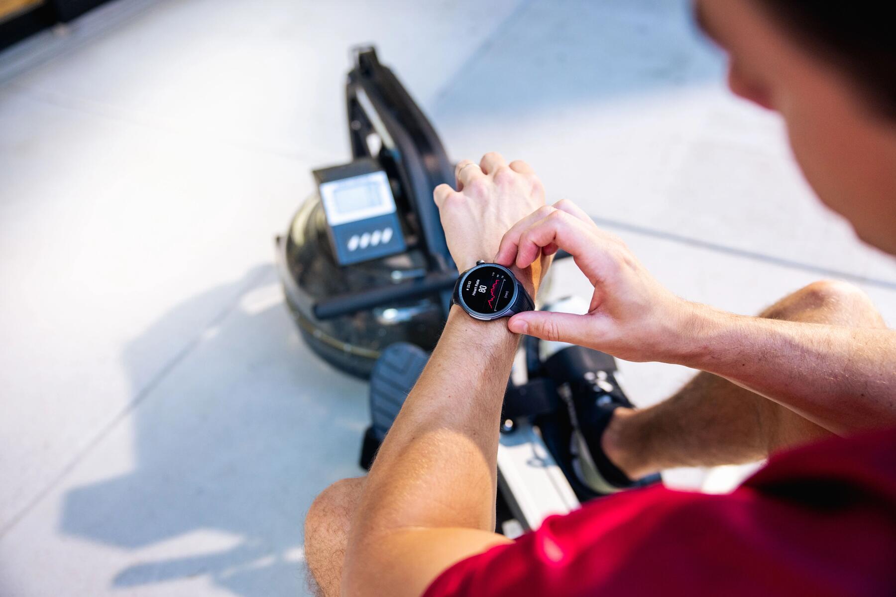 Mężczyzna ćwiczący na rowerze stacjonarnym w pokoju sprawdzajacy smartwatch