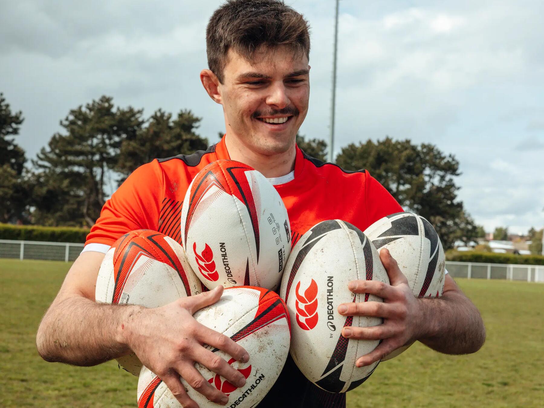 Mężczyzna w stroju do rugby trzymający piłki do rugby stojąc na boisku