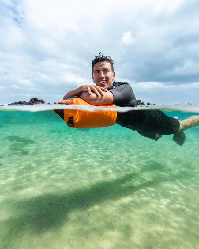 Lächelnder Mann schwimmt im klaren türkisfarbenen Wasser, orangefarbene Boje, Himmel mit Wolken.