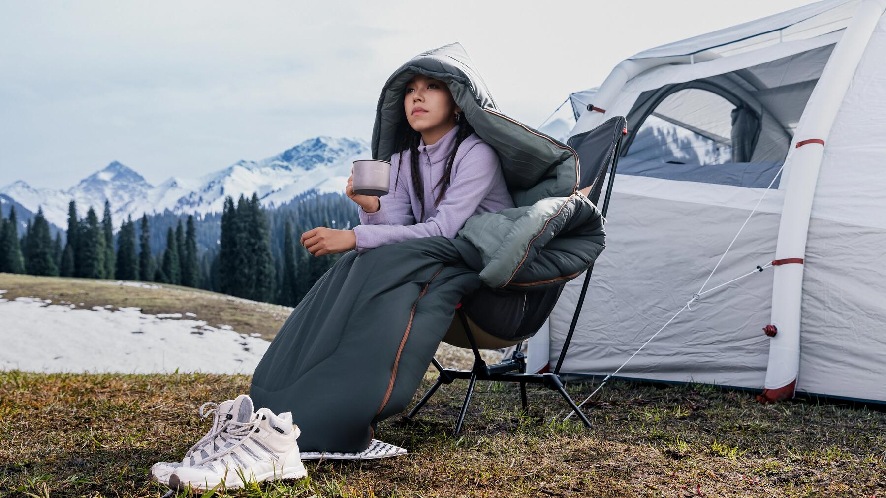 Eine Frau campt im Winter und trinkt Tee vor ihrem Zelt