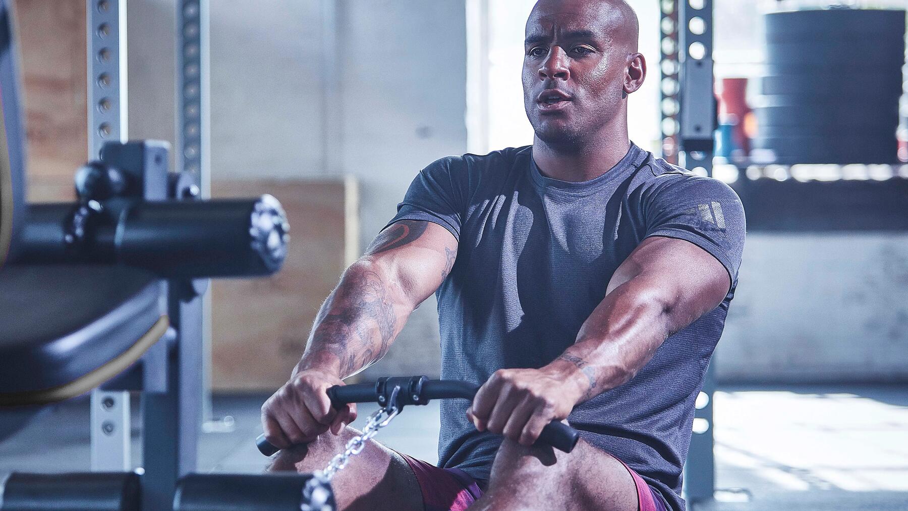 Mann beim Trainieren auf dem Rudergerät in Fintessstudio in dunkler Fitnessbekleidung