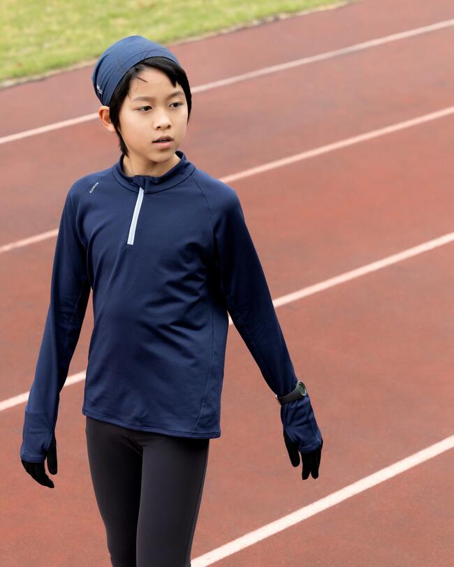 Kind in dunkelblauer Sportkleidung auf roter Laufbahn, grüner Rasen im Hintergrund.