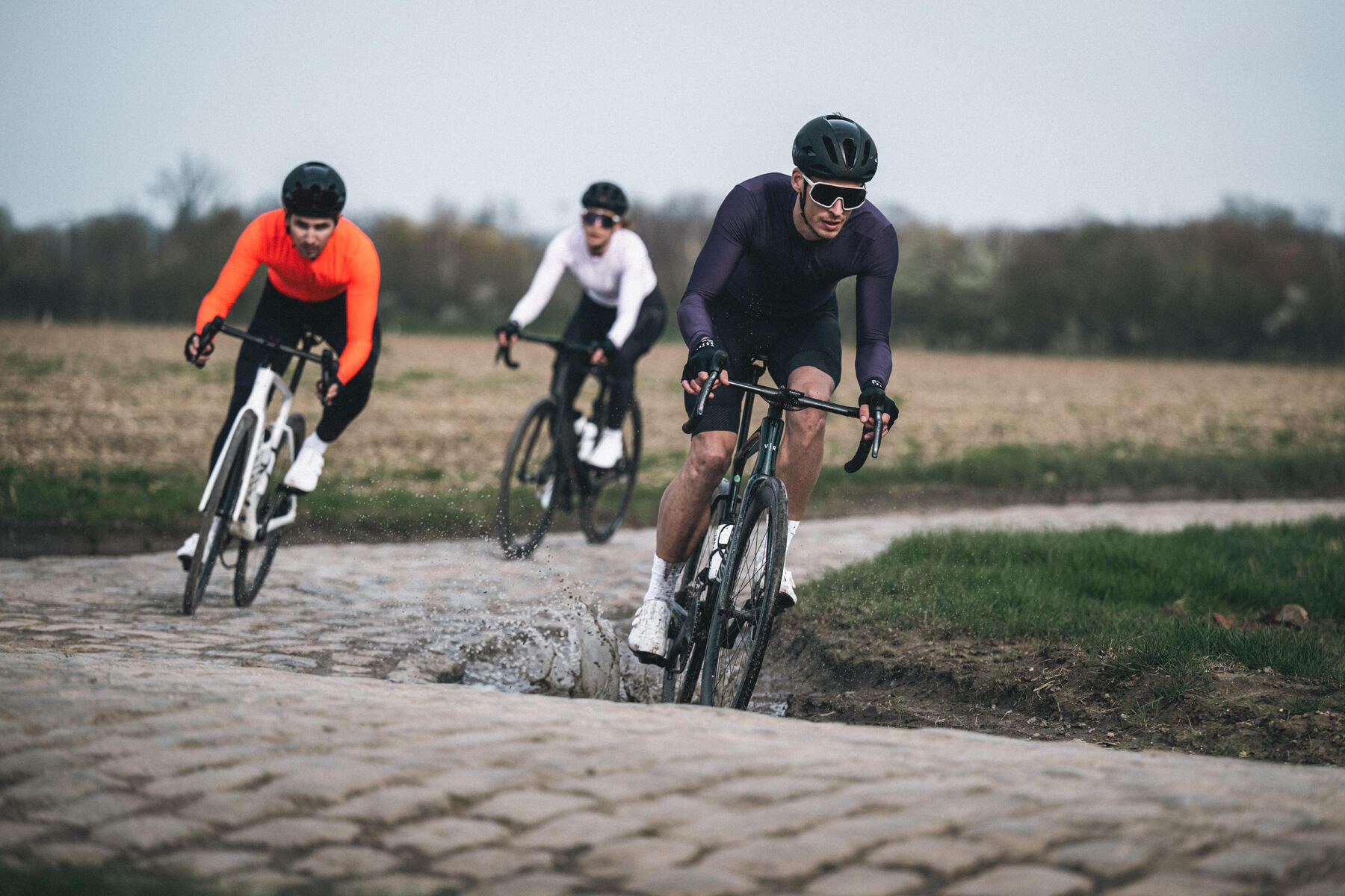 Ludzie w odzieży sportowej kaskach i okularach jadący rowerami po bruku