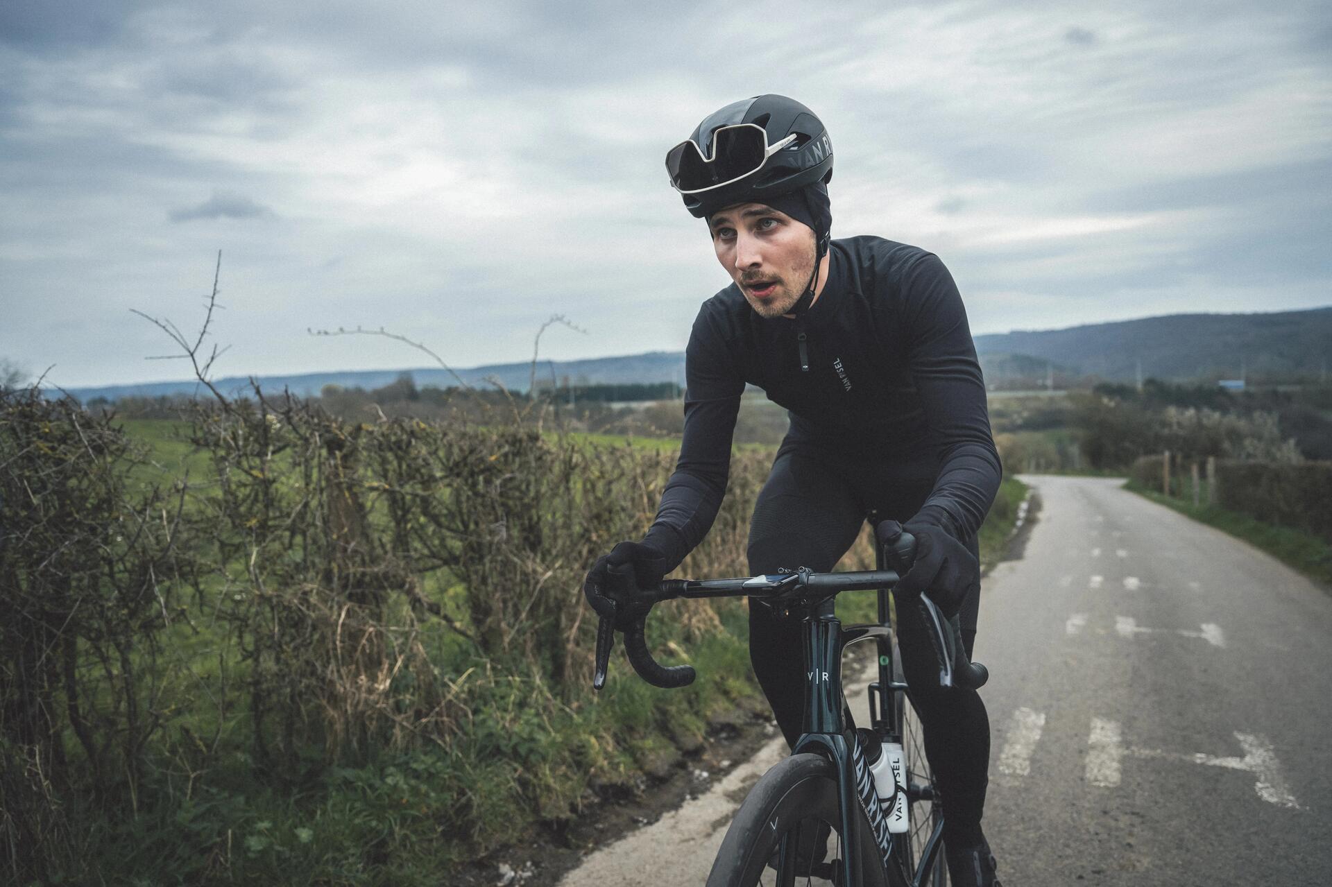 Rowerzysta w kasku i rękawiczkach rowerowych na zimę jadący drogą na rowerze szosowym