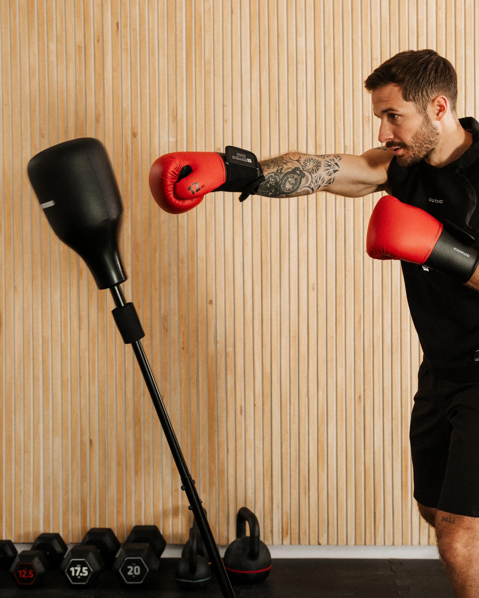 Mann mit roten Boxhandschuhen trainiert an einem stehenden Punchingball in einem privaten Fitnessraum