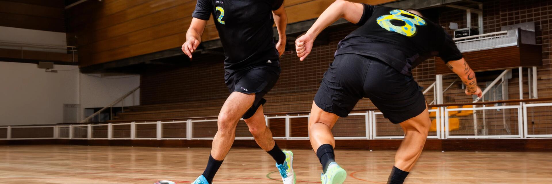 Zwei Männer spielen Futsal in einer Sporthalle, während einer von ihnen mit dem Ball am Fuß an seinem Gegenspieler vorbeidribbelt.