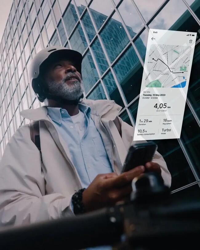 Älterer Mann mit Helm vor gläsernem Hochhaus hält Smartphone, überlagertes Diagramm zeigt Navigationskarte und Daten.