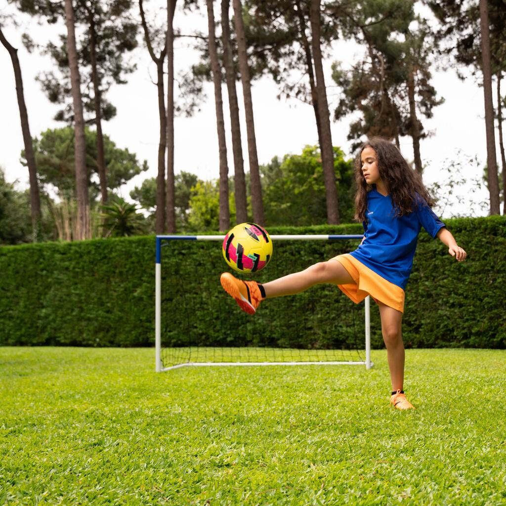 Devojčica se igra fudbalskom loptom ispred fudbalskog gola