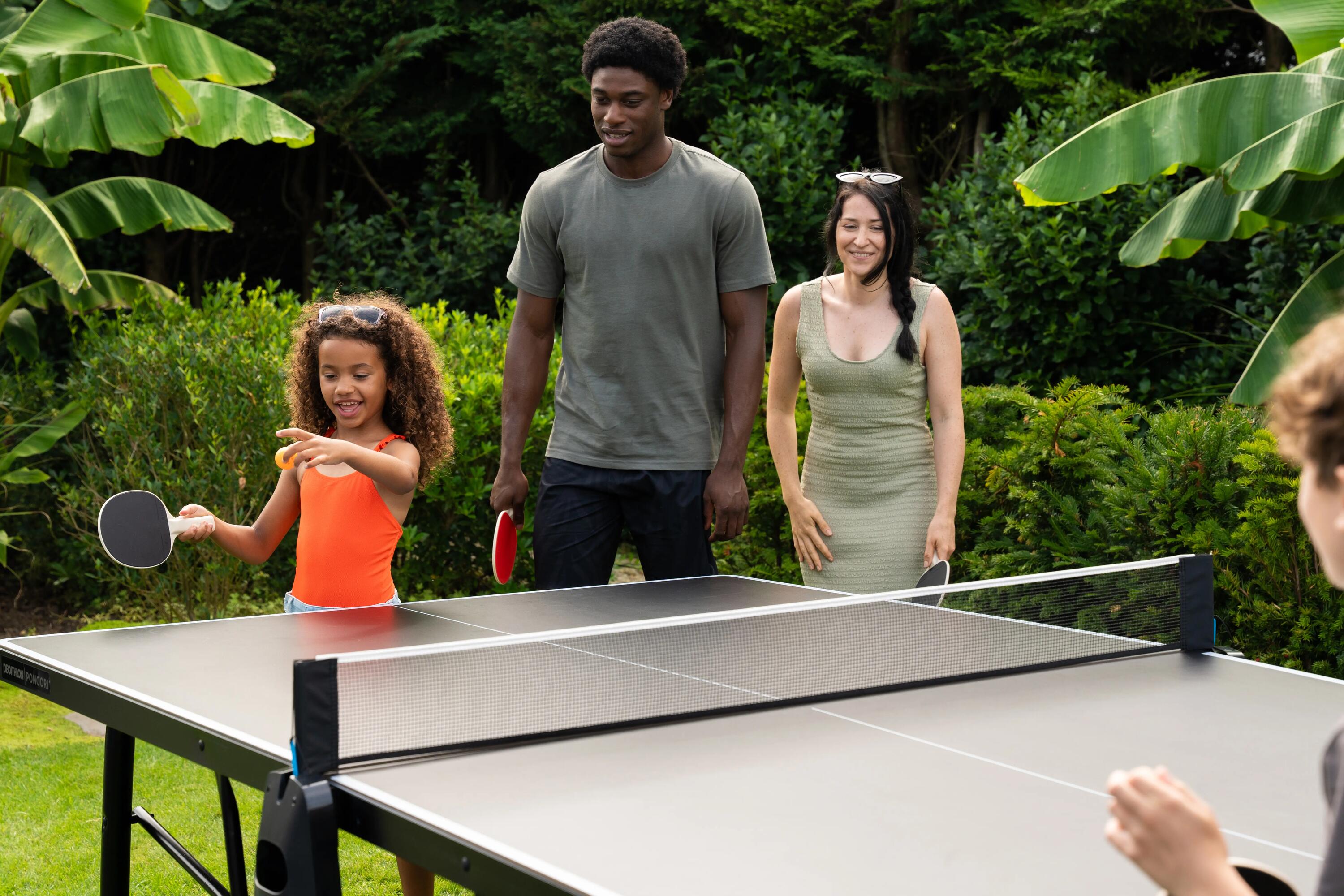 Eine Familie mit einem jungen Mädchen spielt Tischtennis im Garten im Freien.