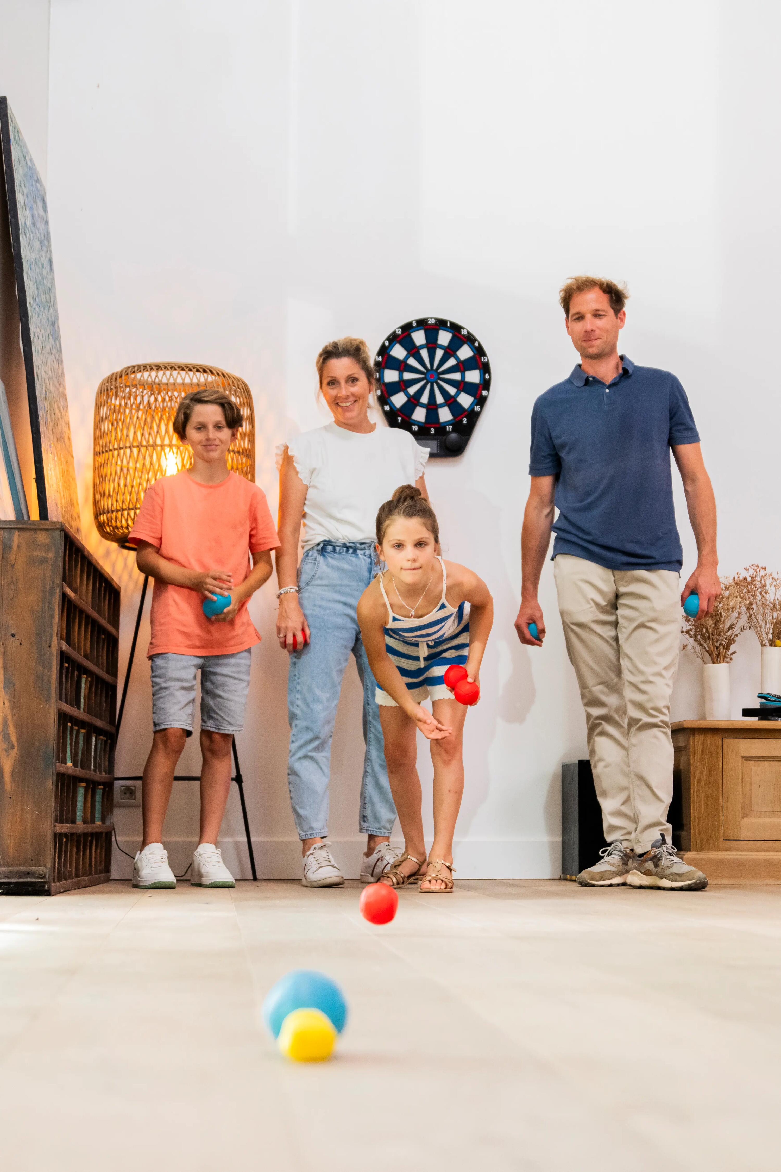 Eine vierköpfige Familie spielt gemeinsam Indoor-Boule im Wohnzimmer, während ein Mädchen eine rote Kugel wirft.