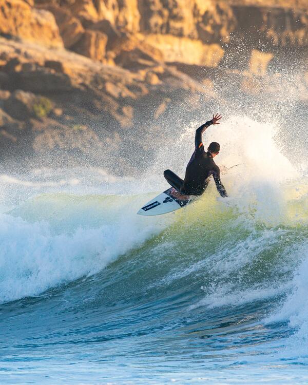 Man springt over een grote golf met zijn surfboard in zijn Decathlon limited edition wetsuit