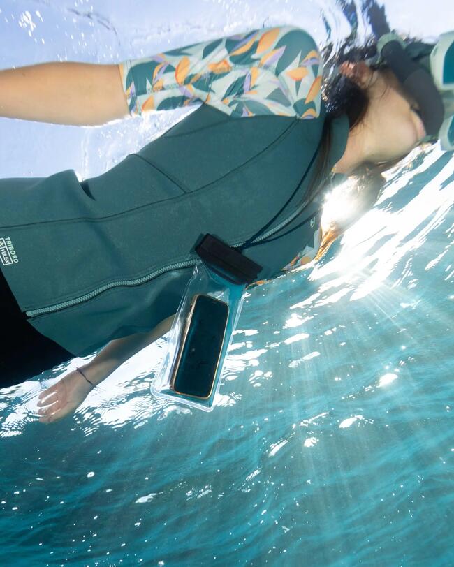 Frau schnorchelt im klaren Wasser, grüner Neoprenanzug, Sonnenstrahlen brechen durch blaue Wellen.