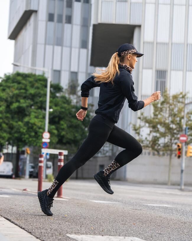 Frau in schwarzer Sportkleidung läuft über eine städtische Straße, umgeben von modernen Gebäuden und grünen Bäumen.