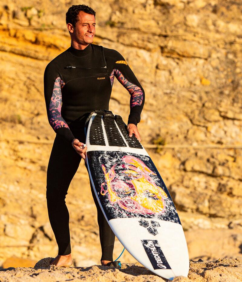 Man staat in limited edition wetsuit op de rotsen naast de zee met zijn surfboard in zijn handen
