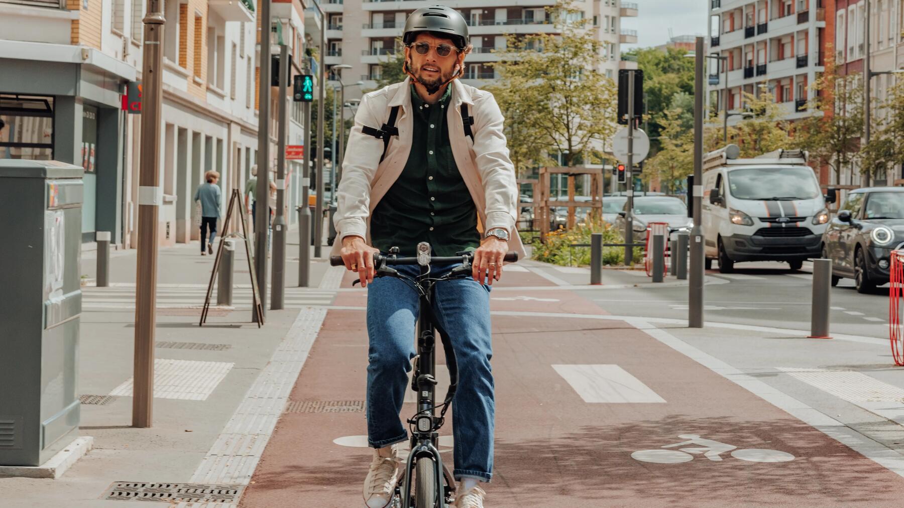 Mężczyzna w kasku rowerowym jadący na rowerze miejskim drogą rowerową w mieście