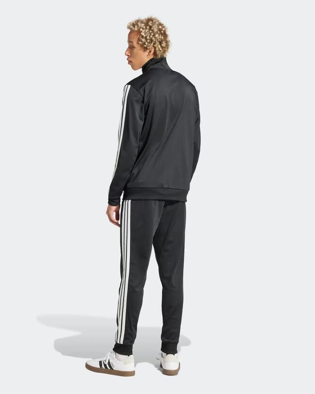 Mann in schwarzem Adidas-Trainingsanzug mit weißen 3-Streifen, von hinten rechts gesehen.