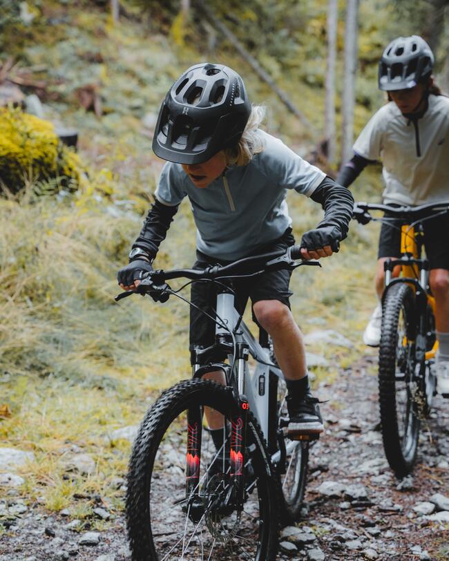 Zwei KInder fahren auf Mountainbikes einen steinigen Waldweg entlang