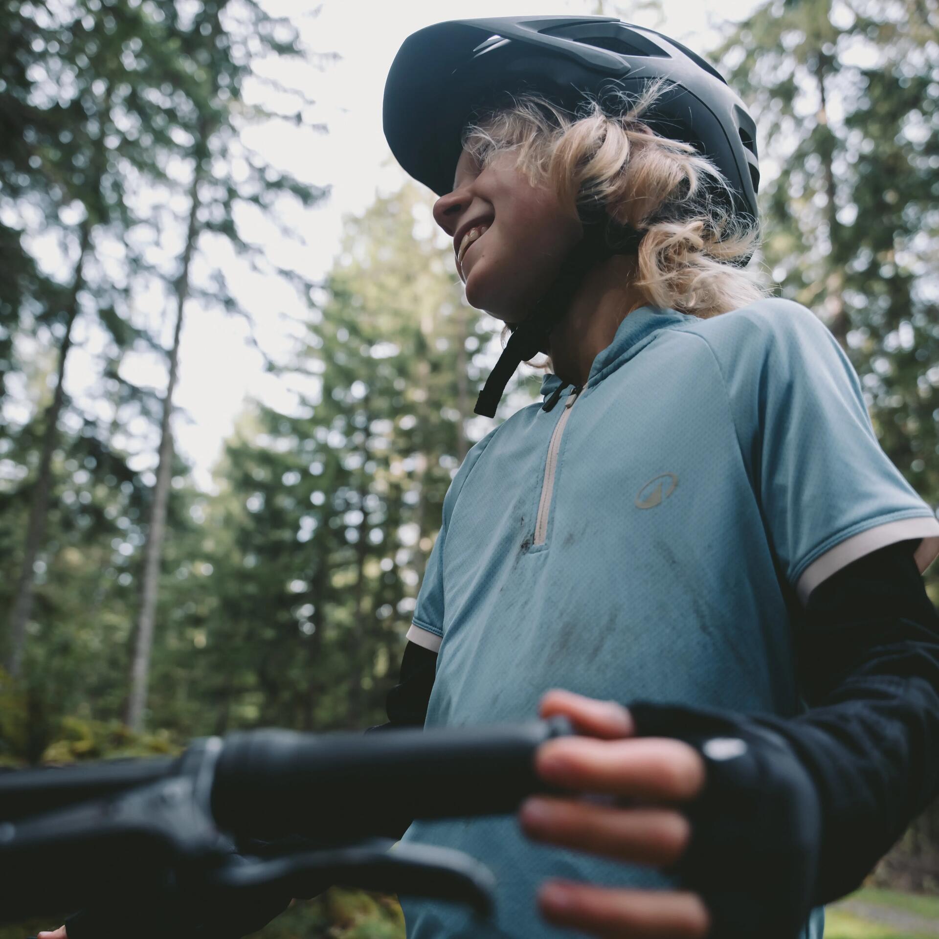 Enfant souriant sur un vtt en forêt portant un casque des gants et un maillot