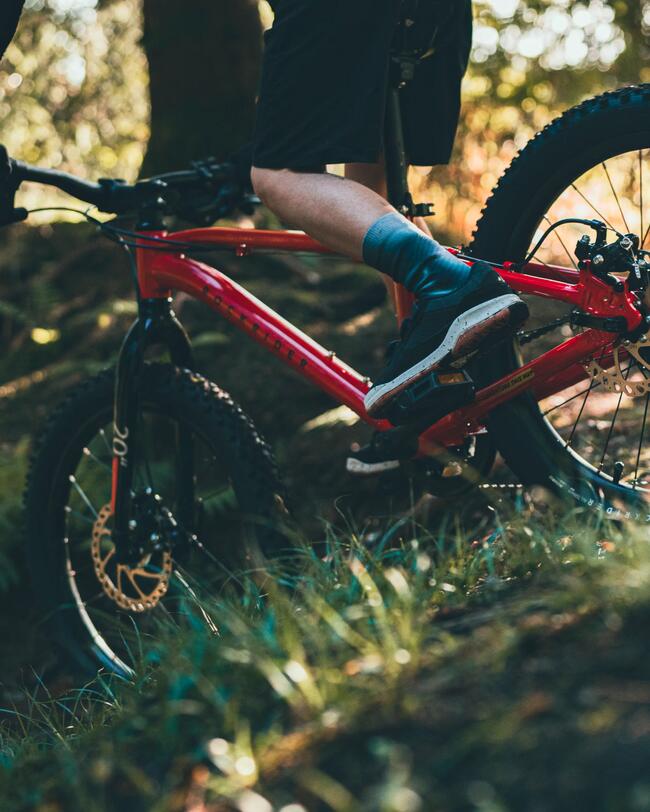 Kind fährt im Stehen auf rotem Mountainbike einen Abhang im Wald hinunter