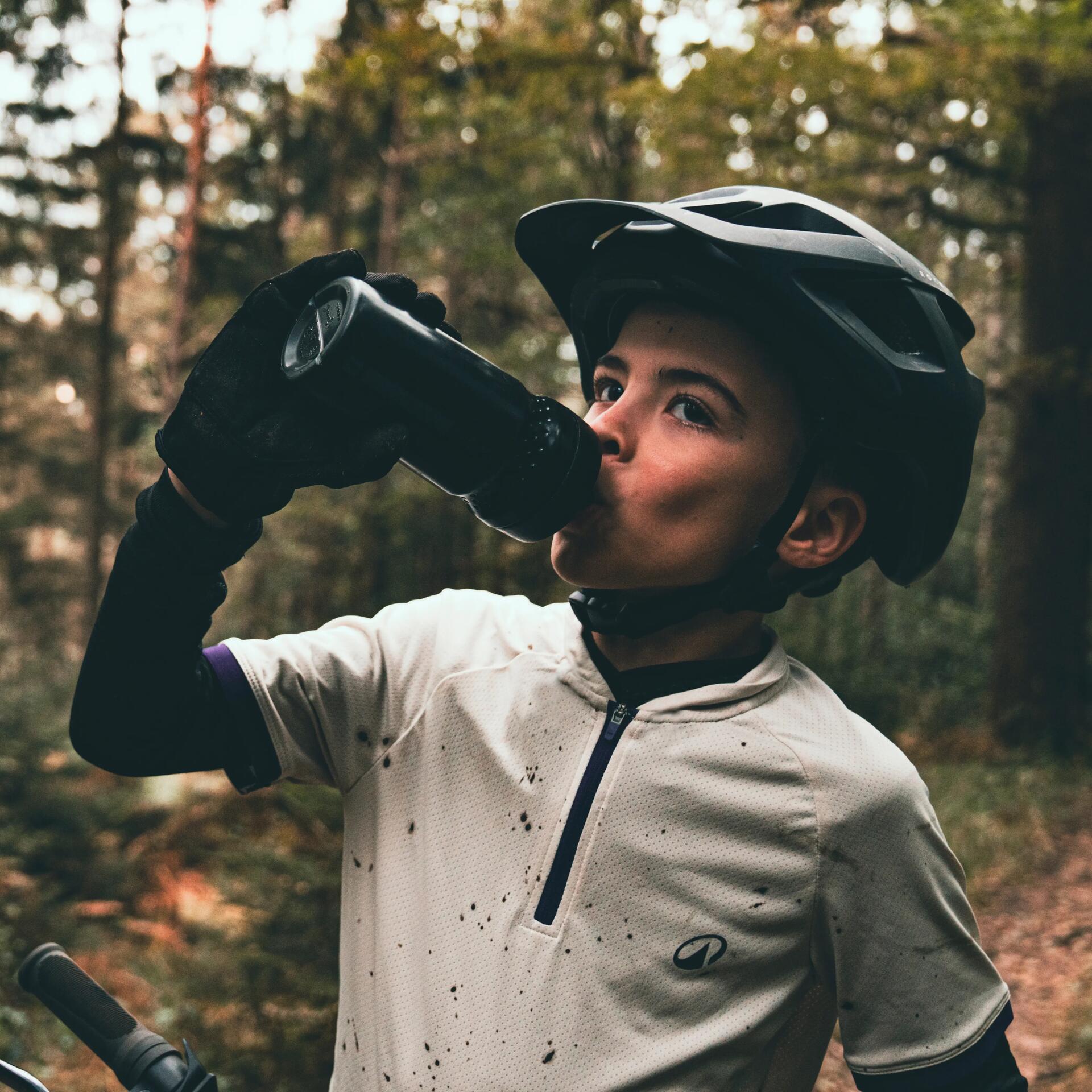 Enfant en vtt dans la forêt portant un casque un maillot et une gourde