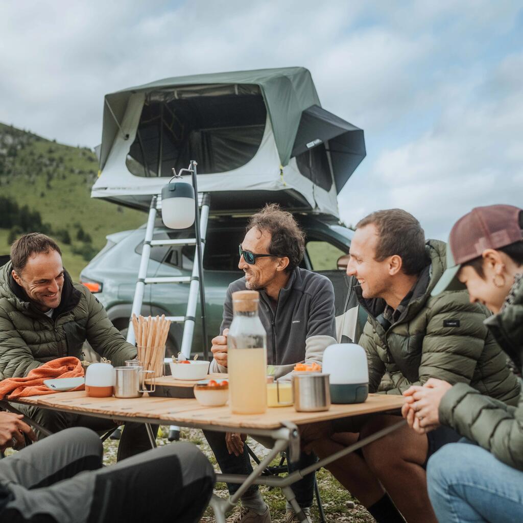 Prijatelji sedijo za mizo in kampirajo s svojim strešnim šotorom na avtomobilu.