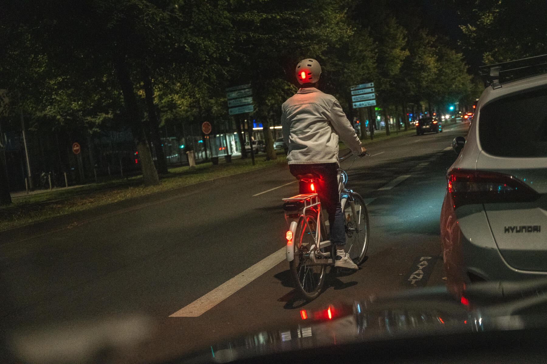 Osoba jadąca w kasku na rowerze po ulicy wieczorową porą