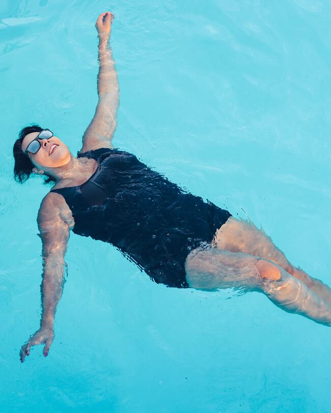 Frau schwimmt im Pool auf dem Rücken, blauer Badeanzug, Sonnenbrille