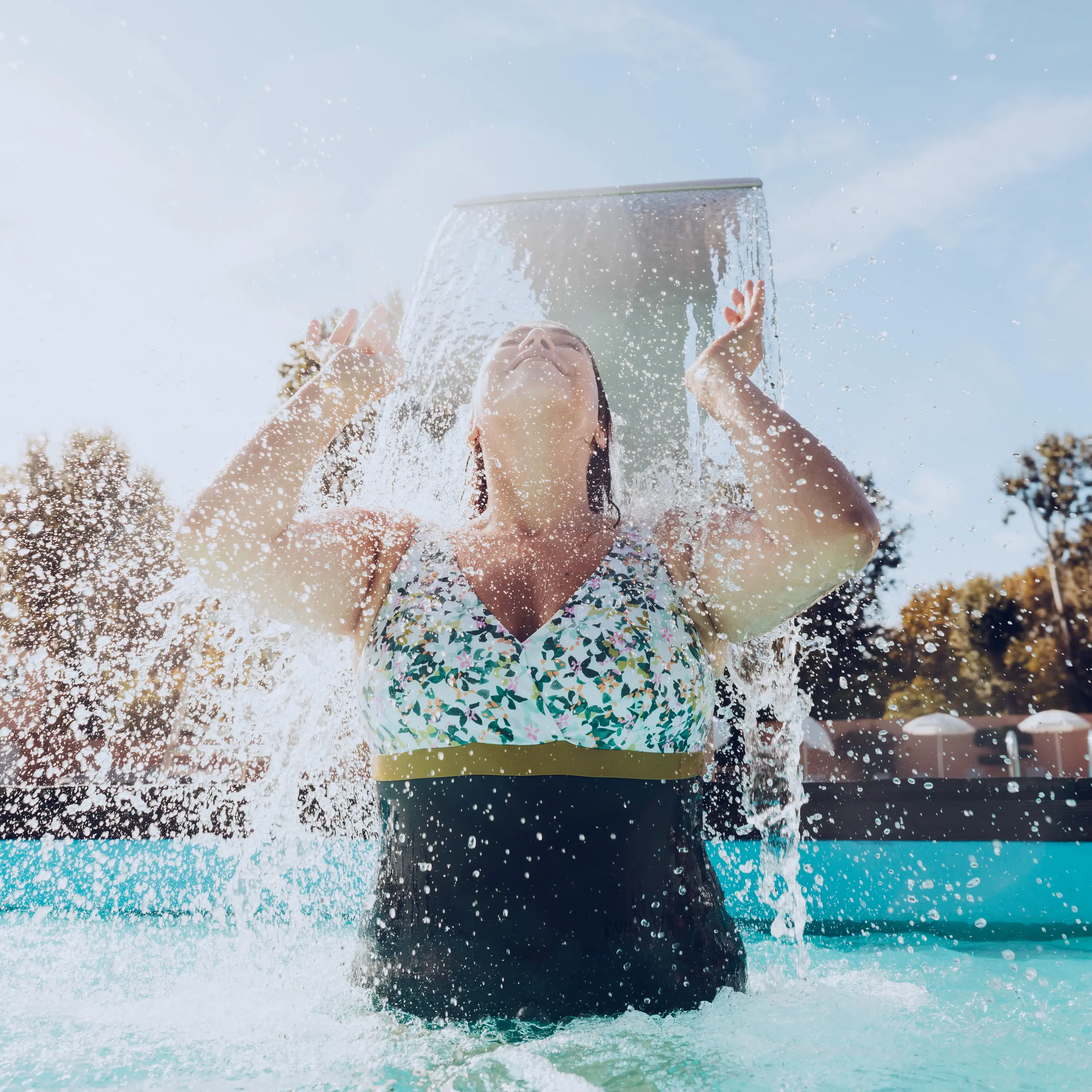 mulher dentro de uma piscina, por baixo de uma cascata de água