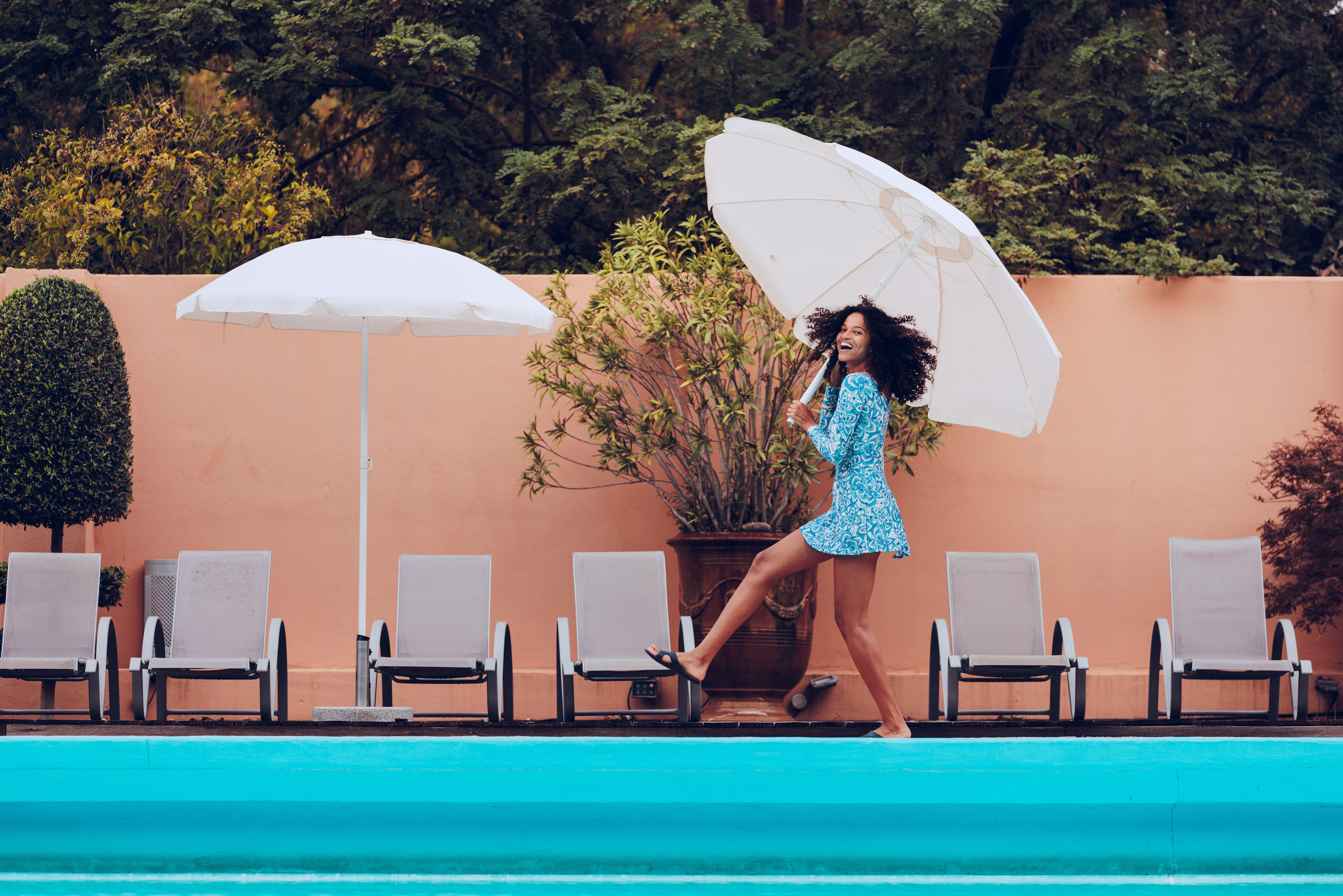 Woman carrying a beach umbrella while wearing a blue swim dress.