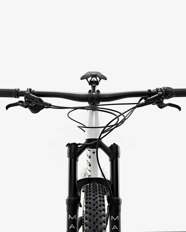 Schwarzes Mountainbike von vorne mit breitem Lenker, grobem Profilreifen und weißem Rahmen auf hellem Hintergrund.