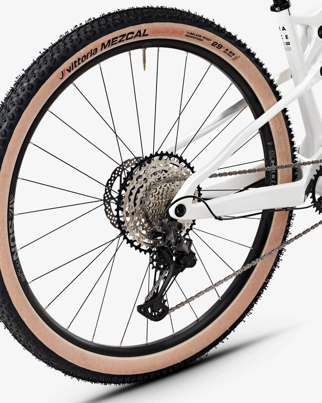 Hinterrad eines weißen Mountainbikes mit beigem Reifen, schwarzer Felge, silberner Kassette und Kette, grobe Reifenstruktur.