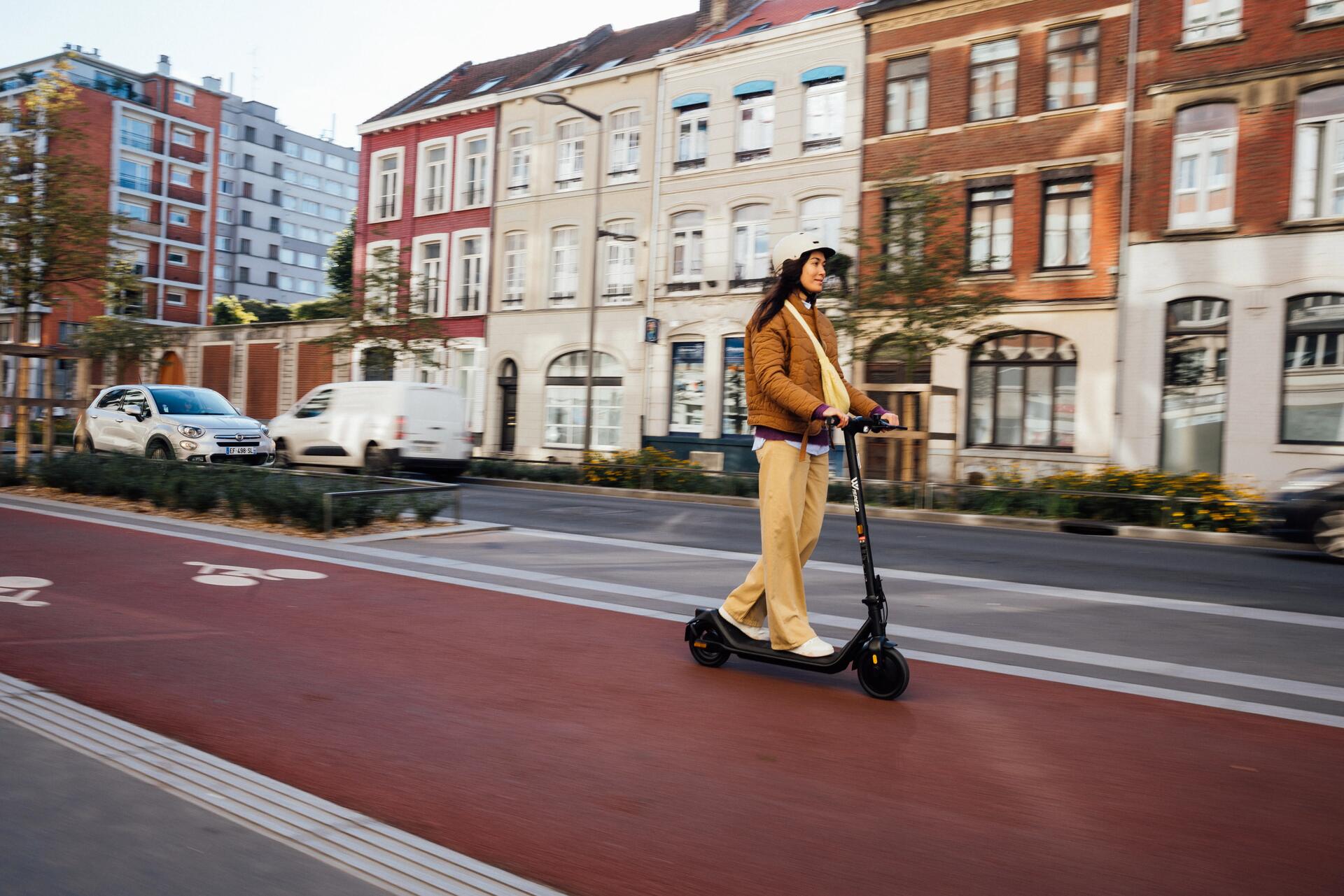 Kobieta w kasku jadąca hulajnogą elektryczną po ścieżce dla rowerów
