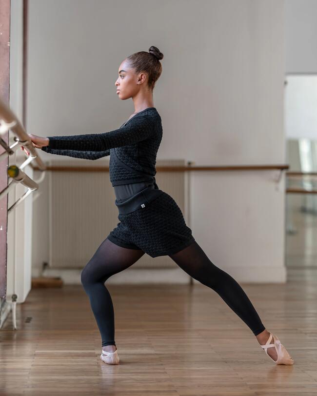 Ein Mädchen wärmt sich an einer Ballettstange auf.