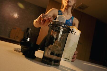 personne sportive qui prépare un shaker de whey proteine