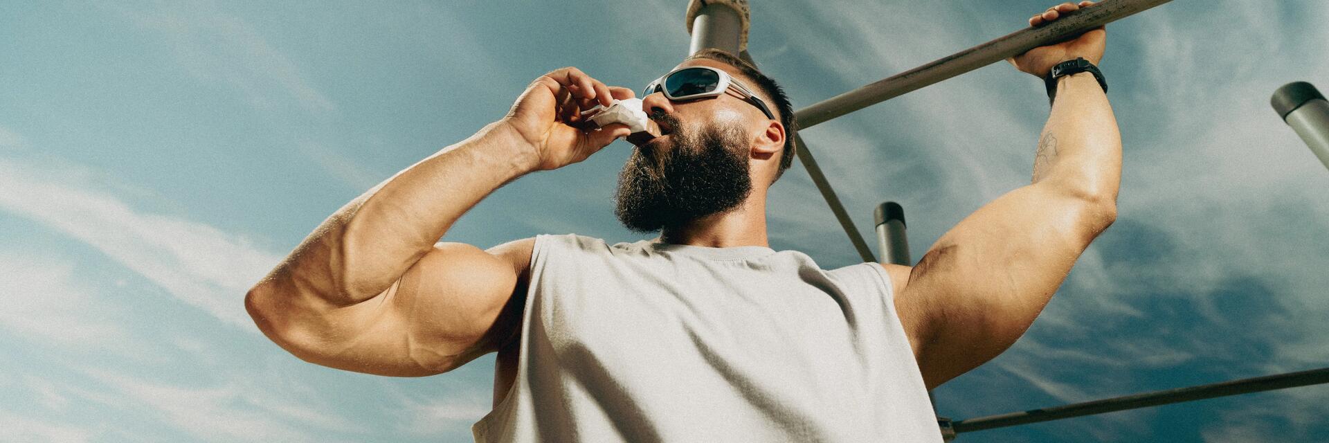 Trainierter Mann ernährt sich bei seiner Cutting Phase proteinreich und hält sich bei Sonne an einer Stange fest