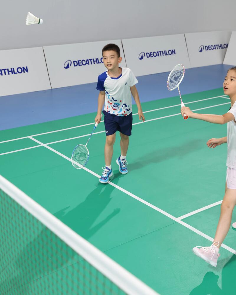 Zwei Kinder spielen in einer Sporthalle Badminton.