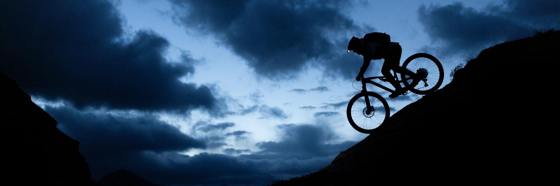 Osoba w kasku z czołówką zjeżdżająca rowerem all mountain z górki nocą