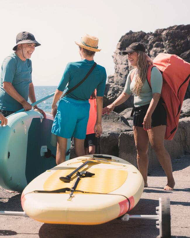 Gruppe von Menschen mit Paddelbrettern am felsigen Ufer vor blauem Meer und klarem Himmel.